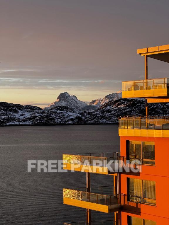 an orange building in the water with mountains in the background at Central Apartment in Bodø with ocean view in Bodø
