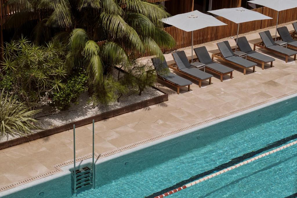 a swimming pool with chairs and palm trees next to it at Las Gaviotas Suites Hotel & Spa in Playa de Muro