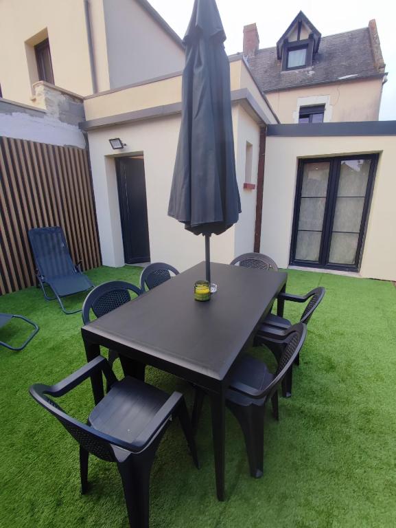 une table avec des chaises et un parasol sur une pelouse dans l'établissement La petite maison de Laura située entre Caen Bayeux la mer, à Bretteville-lʼOrgueilleuse
