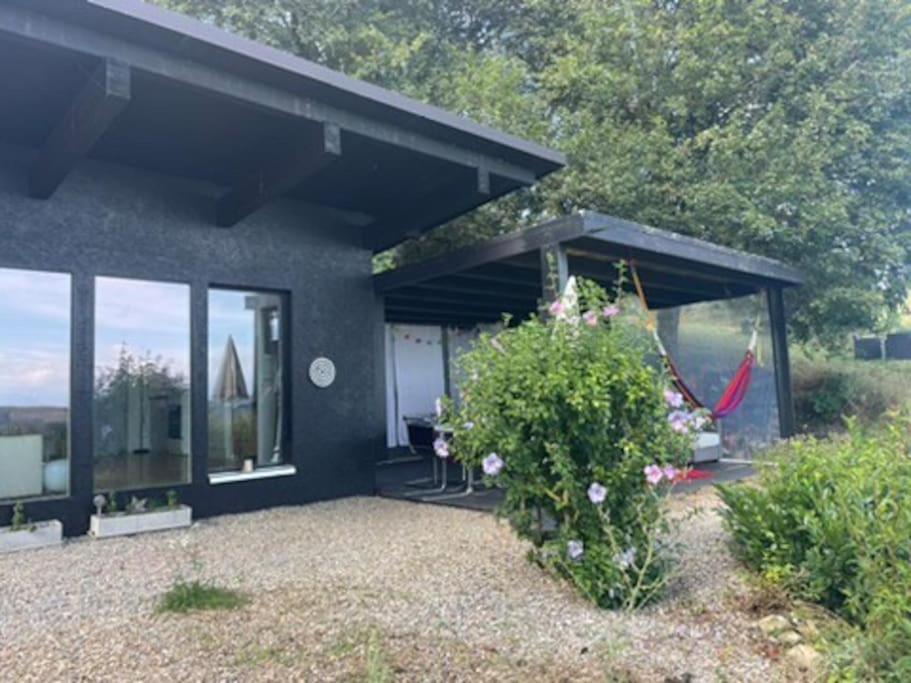 a black house with a patio and a boat in the distance at Graine de Paradis - Tiny House in Le Landeron