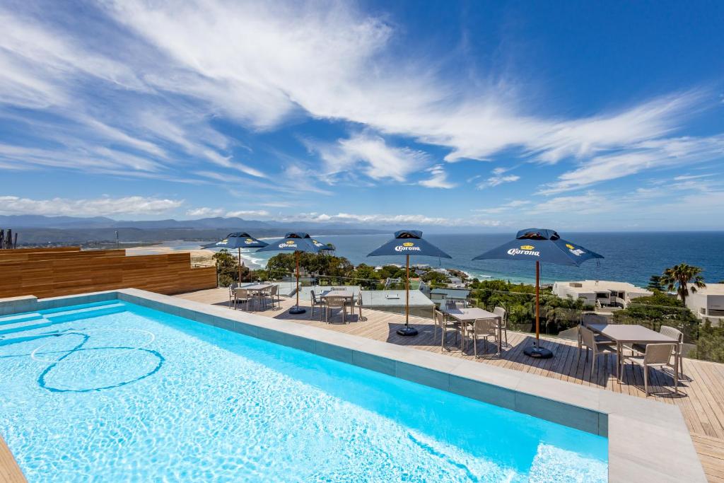 a swimming pool with chairs and umbrellas and the ocean at Plett Quarter Apartments in Plettenberg Bay
