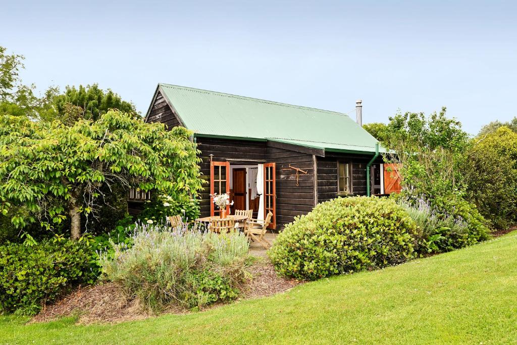 a small wooden house with a green roof at Vineyard Cottages - Kumeu in Waimauku