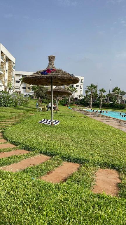 Appartement avec piscine à casa tamaris في دار بوعزة: مظلة من القش موضوعة على العشب بجوار الشاطئ