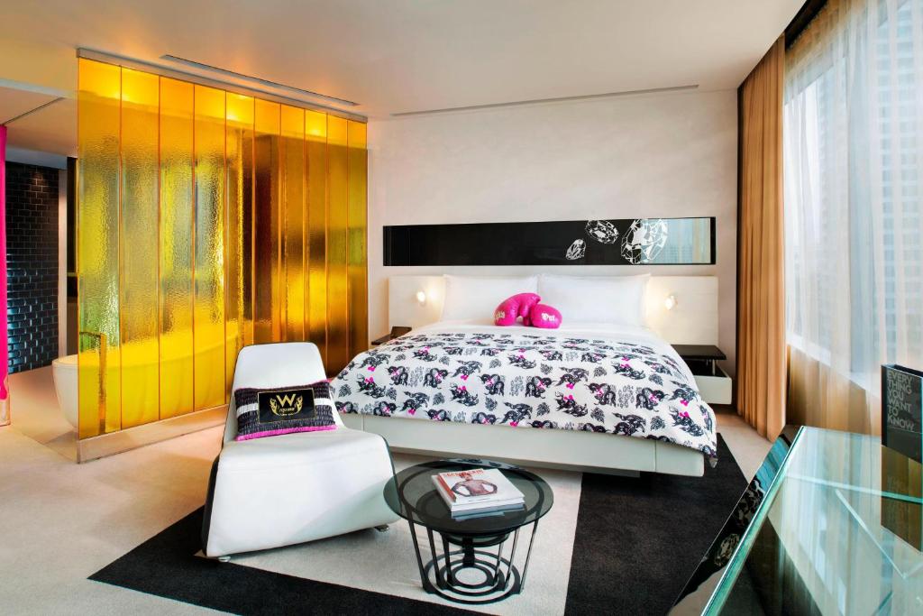 A styled king room with a gold-toned partition, lounge chair and glass-topped table.