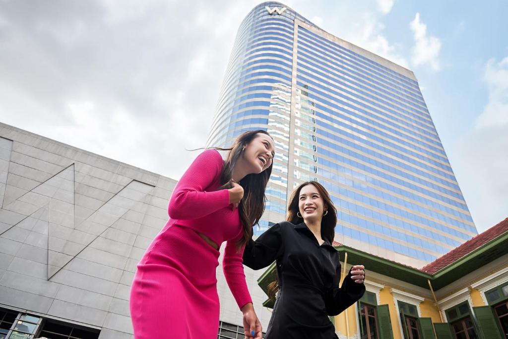 two women dancing in front of a tall building at W Bangkok Hotel in Bangkok