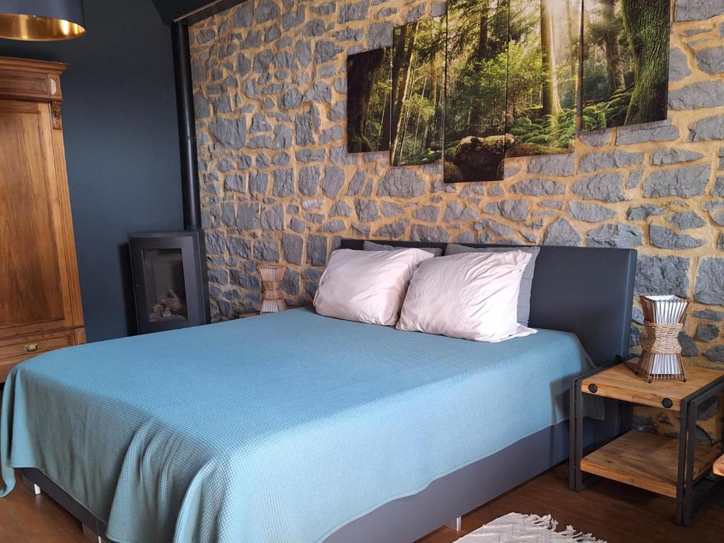 a bedroom with a blue bed with a stone wall at La Laiterie Ecaussinnes in Les Croisettes