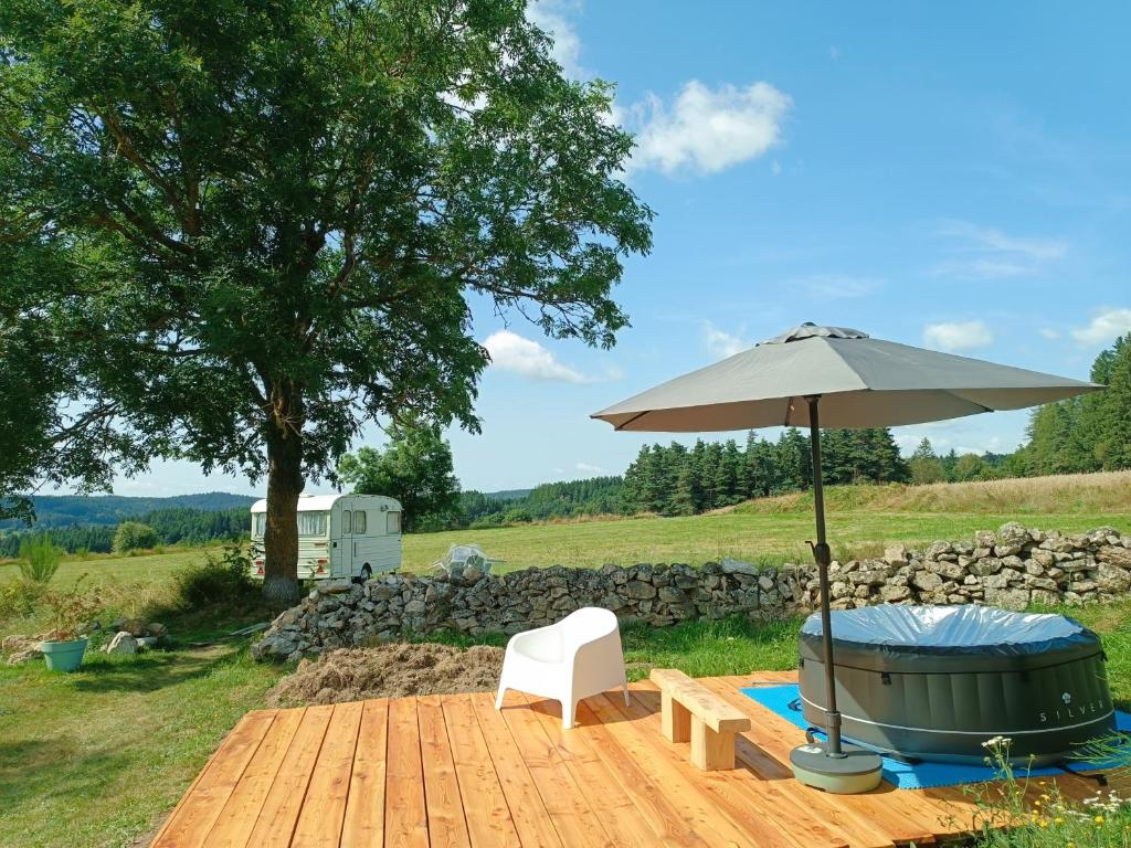 a table with an umbrella and a chair and a hot tub at Caravane Vintage insolite avec jacuzzi au calme in Sauvessanges