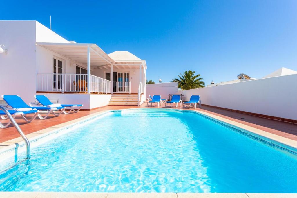 a swimming pool with blue chairs and a house at Villa Adella in Tías