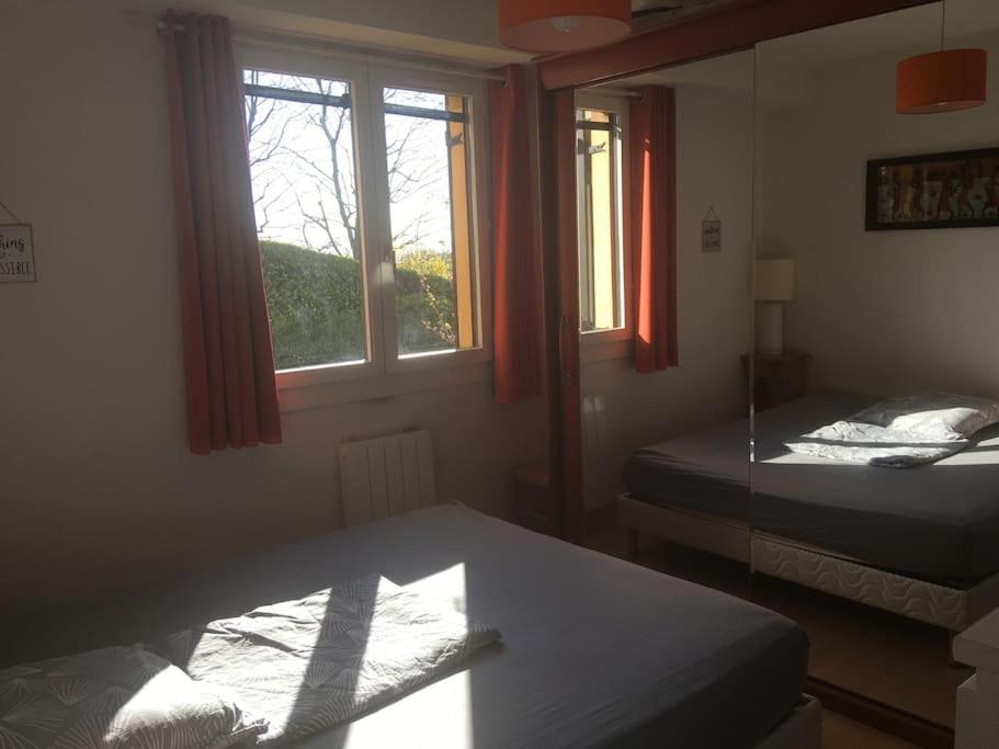 a room with two beds and a table and windows at Appartement en Rez de jardin climatisée 2 pièces-cuisine avec terrasse et jardin in Sainte-Foy-lès-Lyon