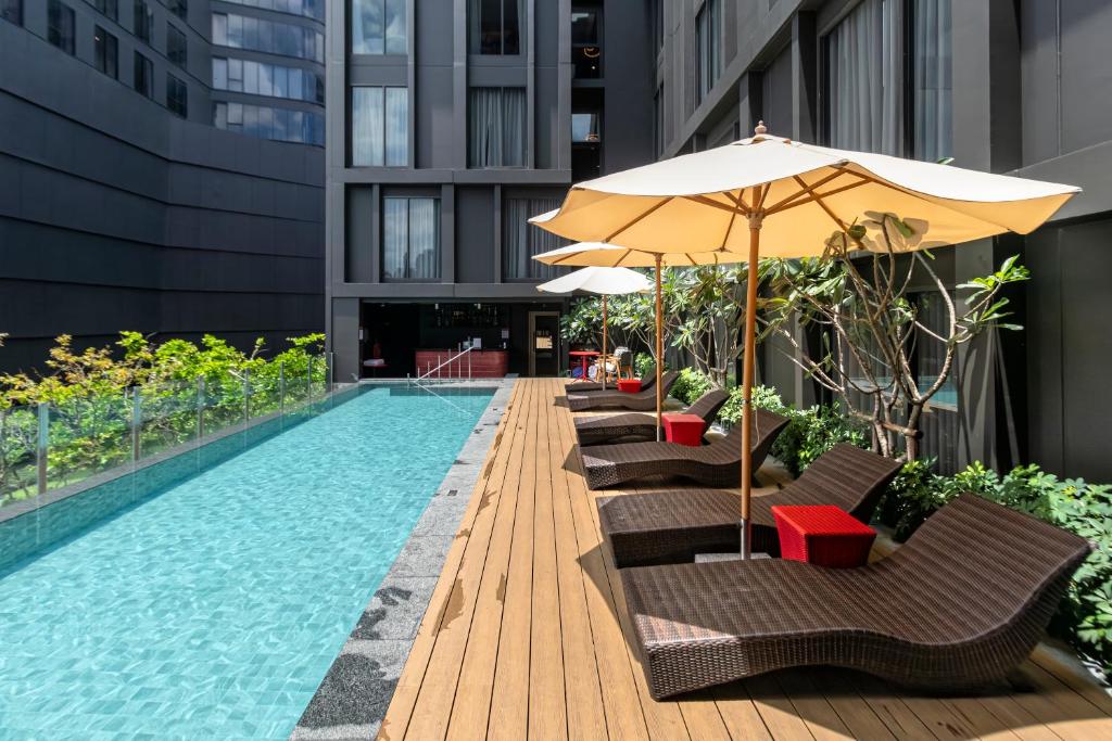 a pool with chairs and an umbrella next to a building at Oakwood Studios Sukhumvit Bangkok in Bangkok