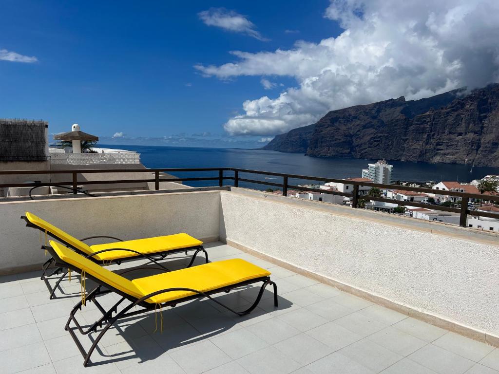 プエルト・デ・サンティアゴにあるRoom in 4 bedroom penthouse with stunning patioの海を見下ろすバルコニーに置かれた2つの黄色いラウンジチェア