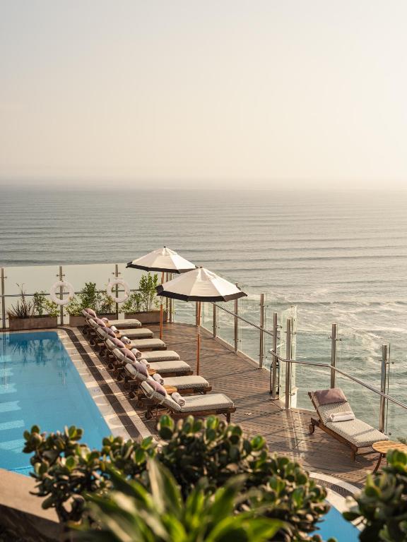 a pool with chairs and umbrellas next to the ocean at Miraflores Park, A Belmond Hotel, Lima in Lima