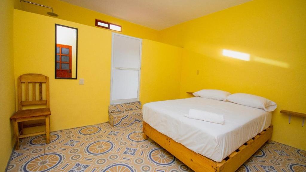 a yellow bedroom with a bed and a chair at La Playa hostel in Mazunte