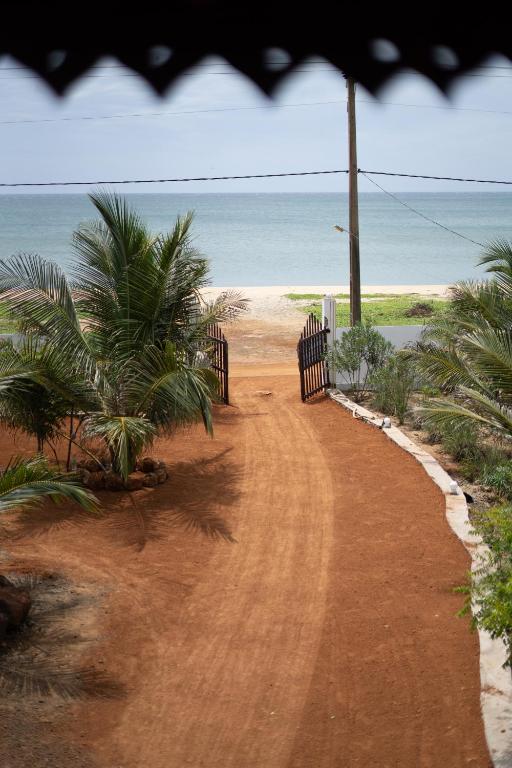 a dirt road leading to a beach with palm trees at Banyan Beach Cottage SRI LANKA in Kalapu