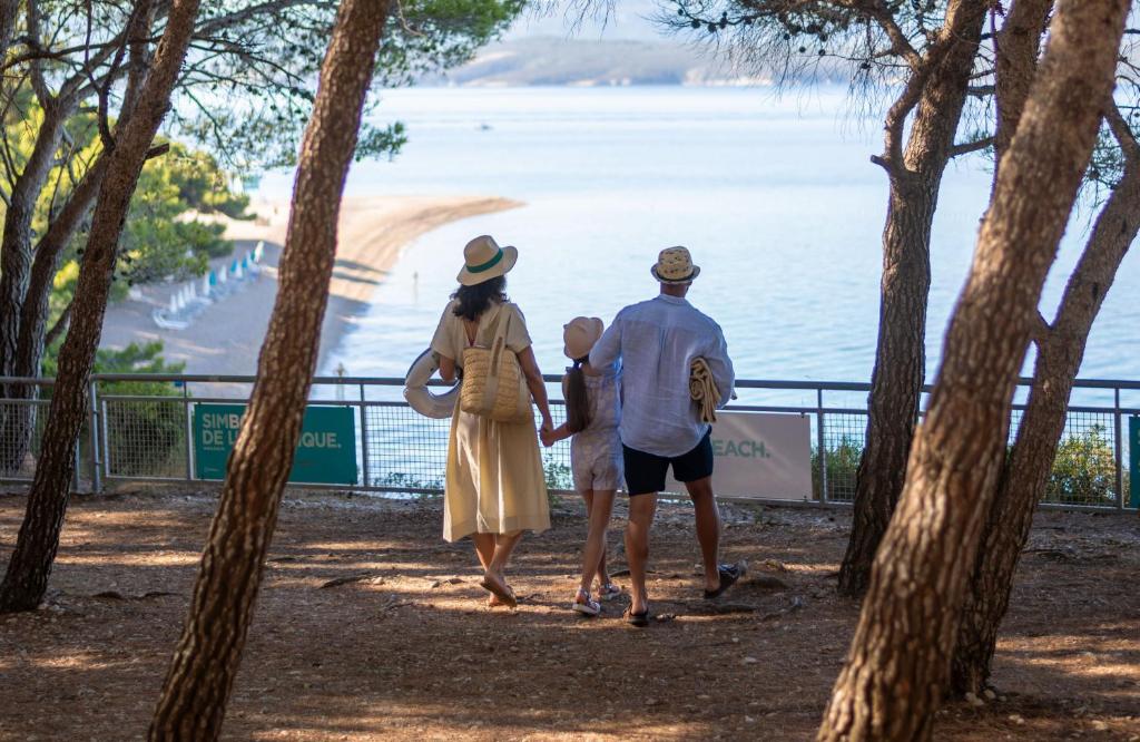 a family walking through the trees near the water at Bluesun Holiday Village Bonaca - Full Board Plus in Bol