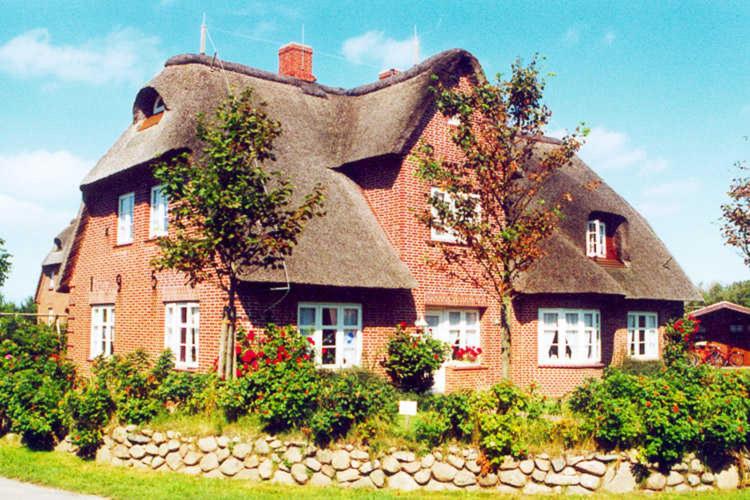 ein strohgedecktes Haus mit einem Steinzaun davor in der Unterkunft Meeresbrise, Whg EG, Otto Guatingwai 18 in Goting