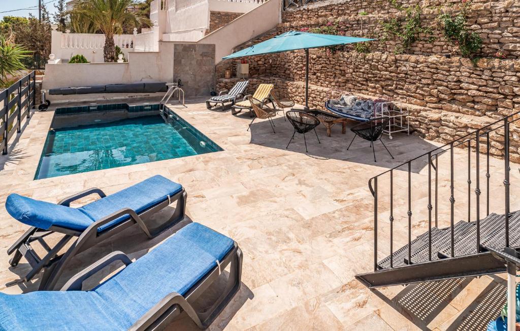 Una piscina con sillas azules, una mesa y una sombrilla. en Lovely Home In San Juan De Los Terreros, en San Juan de los Terreros