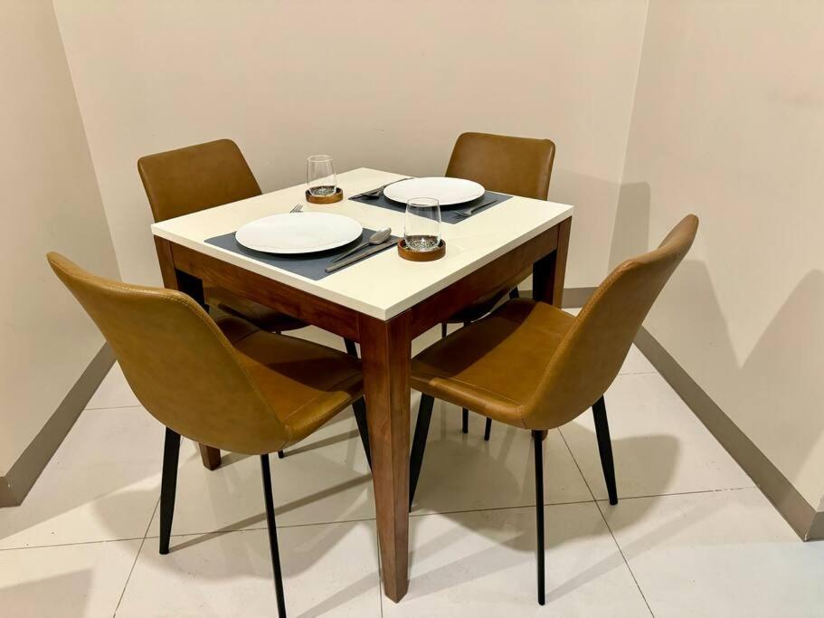 a dining room table with four chairs and a white table and plates at BGC 1BR unit linked to Uptown Mall with own parking in Manila