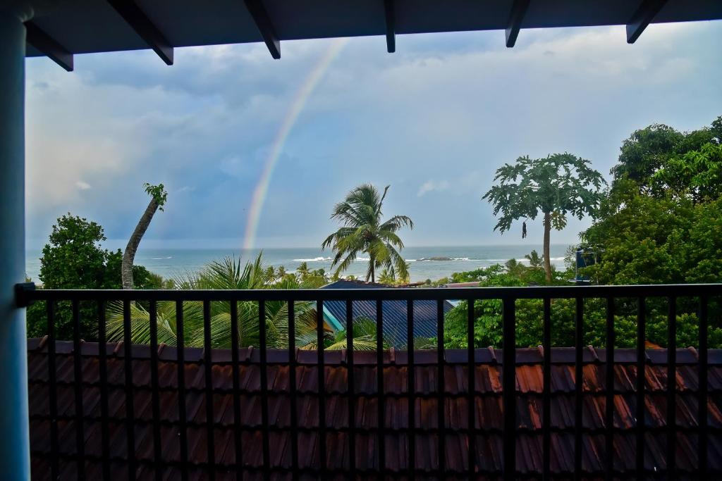 a rainbow over the ocean with a fence and trees at Sandun Villas in Unawatuna