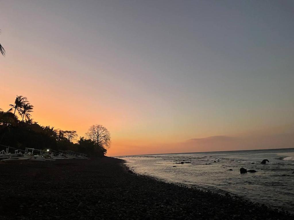 a sunset on a beach with palm trees and the ocean at Bali Dream House in Amed