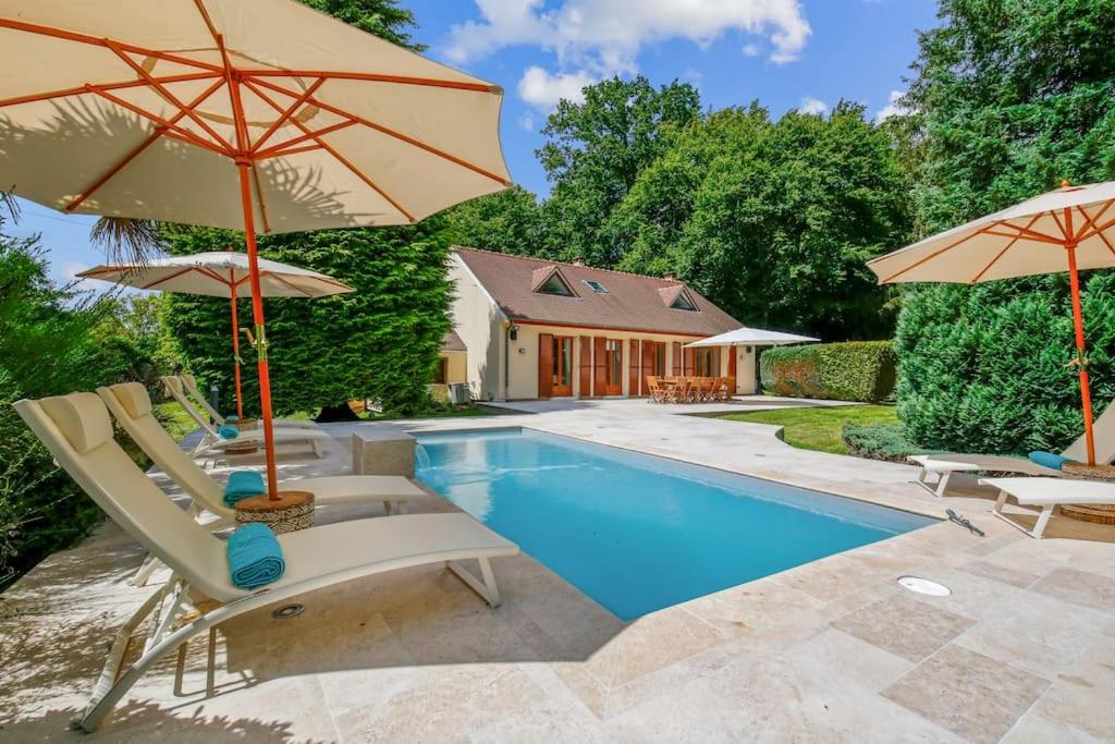 a pool with chairs and umbrellas next to a house at Magnifique Villa, 1H de Paris, Piscine chauffée ! in Labosse