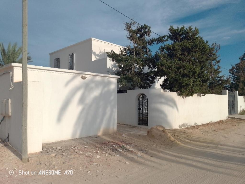 a white building with a gate on a dirt road at Maison La rose 1 in Mezraya