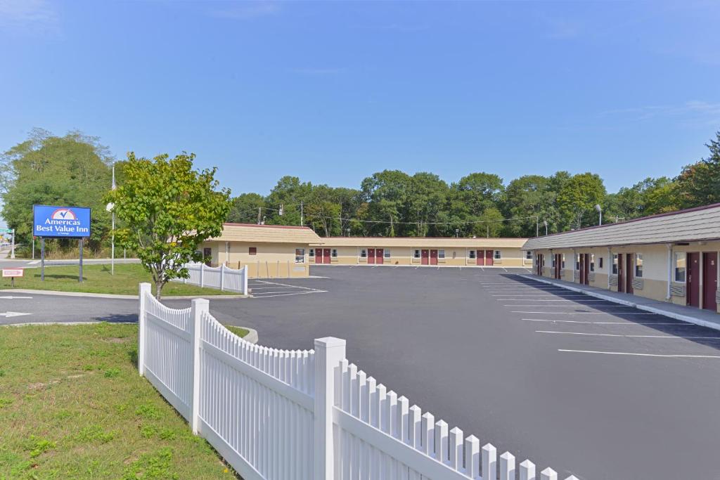 a parking lot with a white fence in front of a building at Americas Best Value Inn - Port Jefferson Station - Long Island in Port Jefferson Station