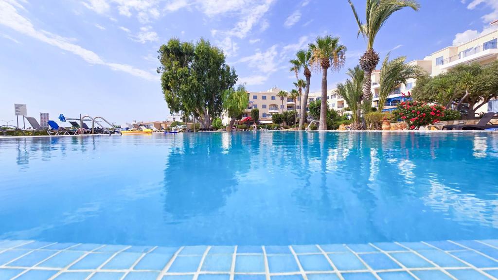 a large swimming pool with blue water and palm trees at CSS Cute Superior King's Palace in Paphos City