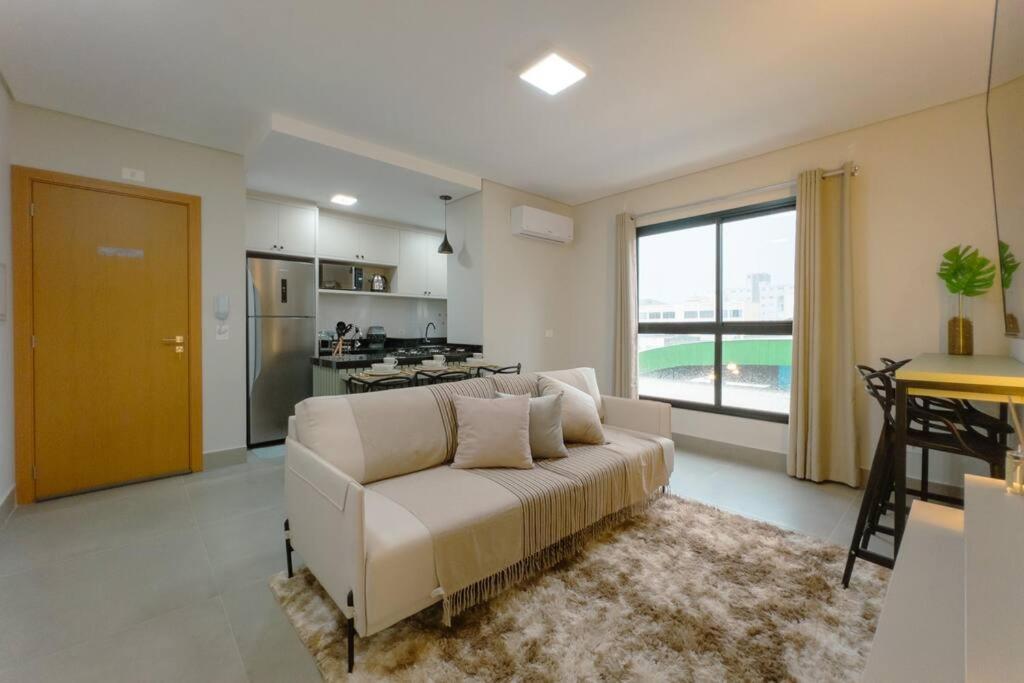 a living room with a white couch and a kitchen at Lindo Moderno e Central TV102 in Maringá