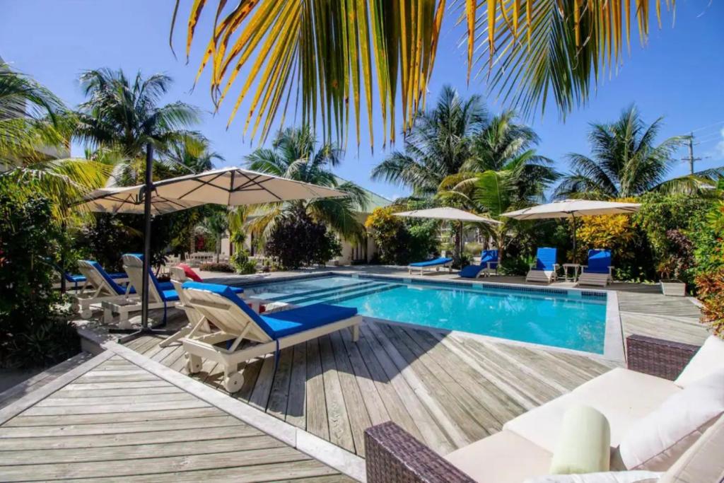 una piscina en un resort con sillas y sombrillas en Belize Beachfront Apartment, en San Pedro