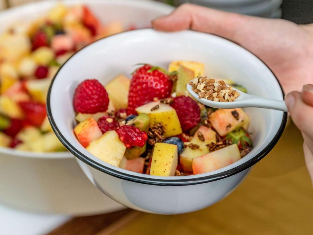 a person holding a bowl of fruit with a spoon at ibis Pune Viman Nagar - An Accor Brand in Pune