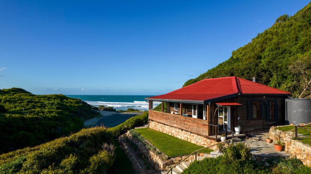 una casa con techo rojo en una colina en Milkwood Cottage - Seaview Serenity, en Sedgefield