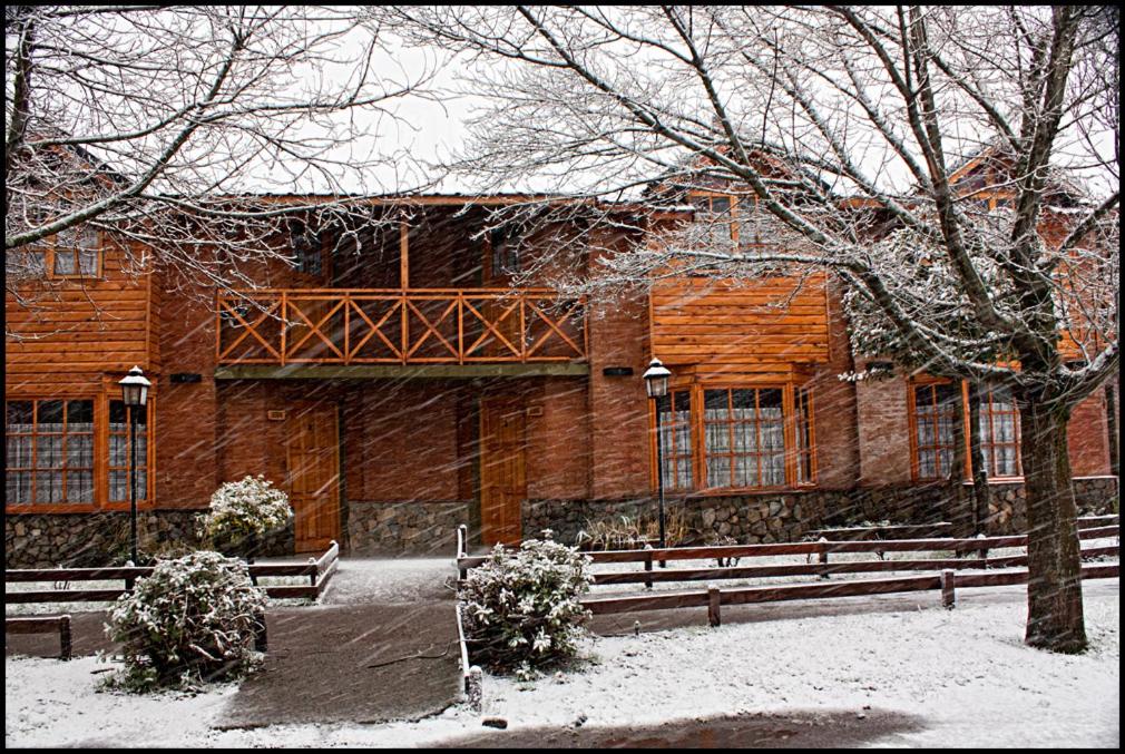 un edificio cubierto de nieve con bancos delante en Cabaña Albar en San Martín de los Andes