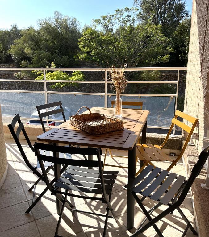 une table en bois avec des chaises et un panier sur un balcon dans l'établissement SAINT FLORENT - T3 Climatisé piscine FLO147, à Saint-Florent