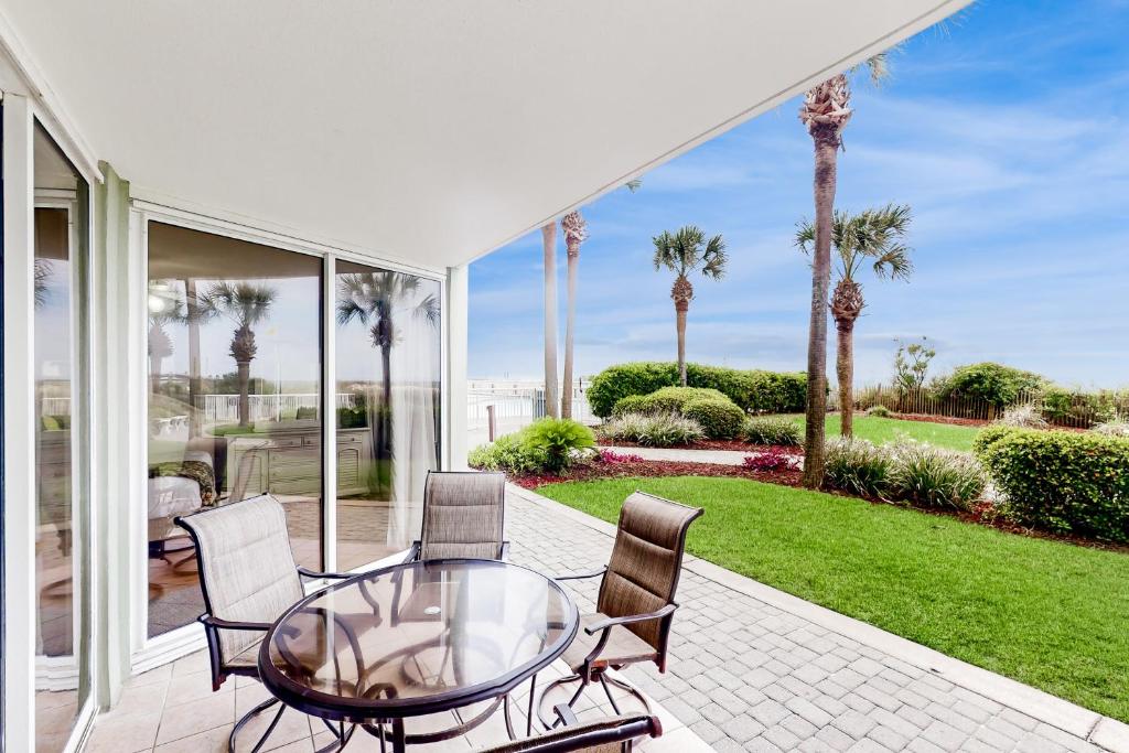 Una mesa de cristal y sillas en un patio con palmeras. en Waters Edge 105, en Fort Walton Beach
