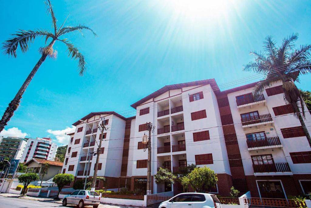 Dos palmeras y un edificio con coches aparcados delante. en Apartamento Águas de Lindoia, en Águas de Lindóia