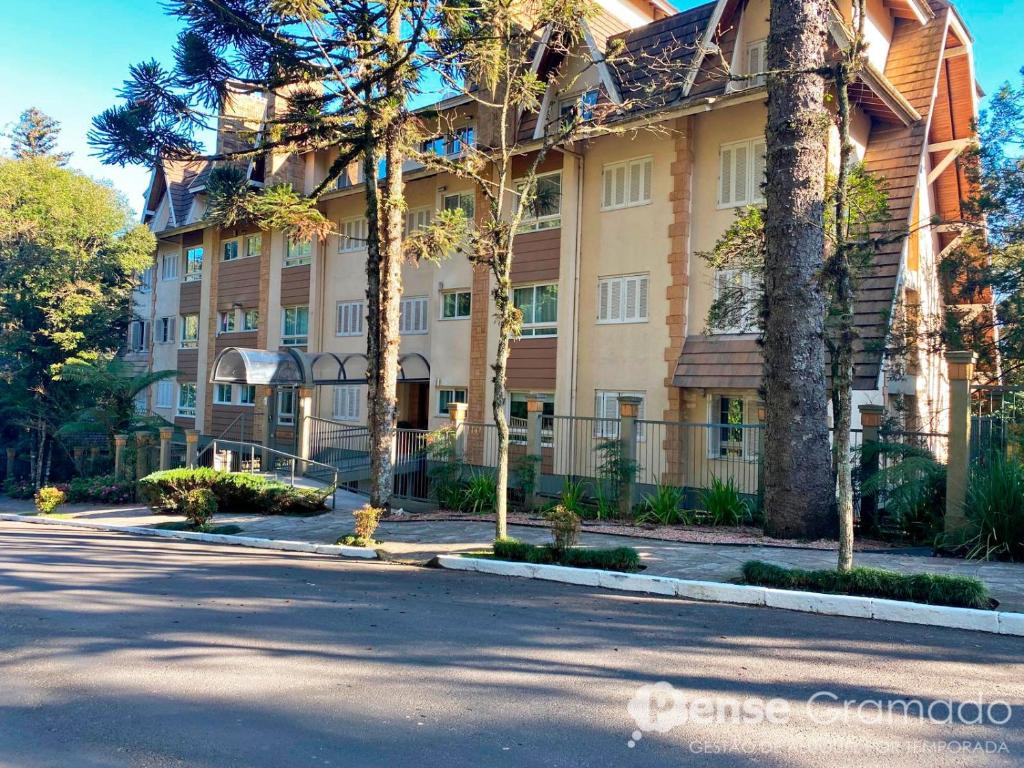 a large building with palm trees in front of a street at Apartamento 1 dormitório a 150m do Mini Mundo in Gramado