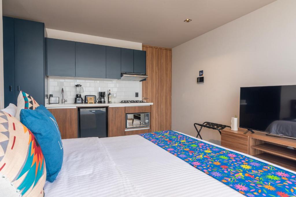 A studio bedroom viewed toward its kitchenette and television.