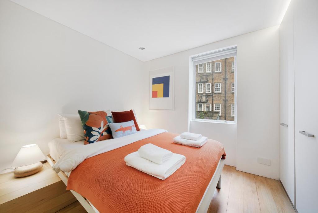 a white bedroom with a large bed with orange blanket at Fitzrovia Apartment By Morethanstays in London