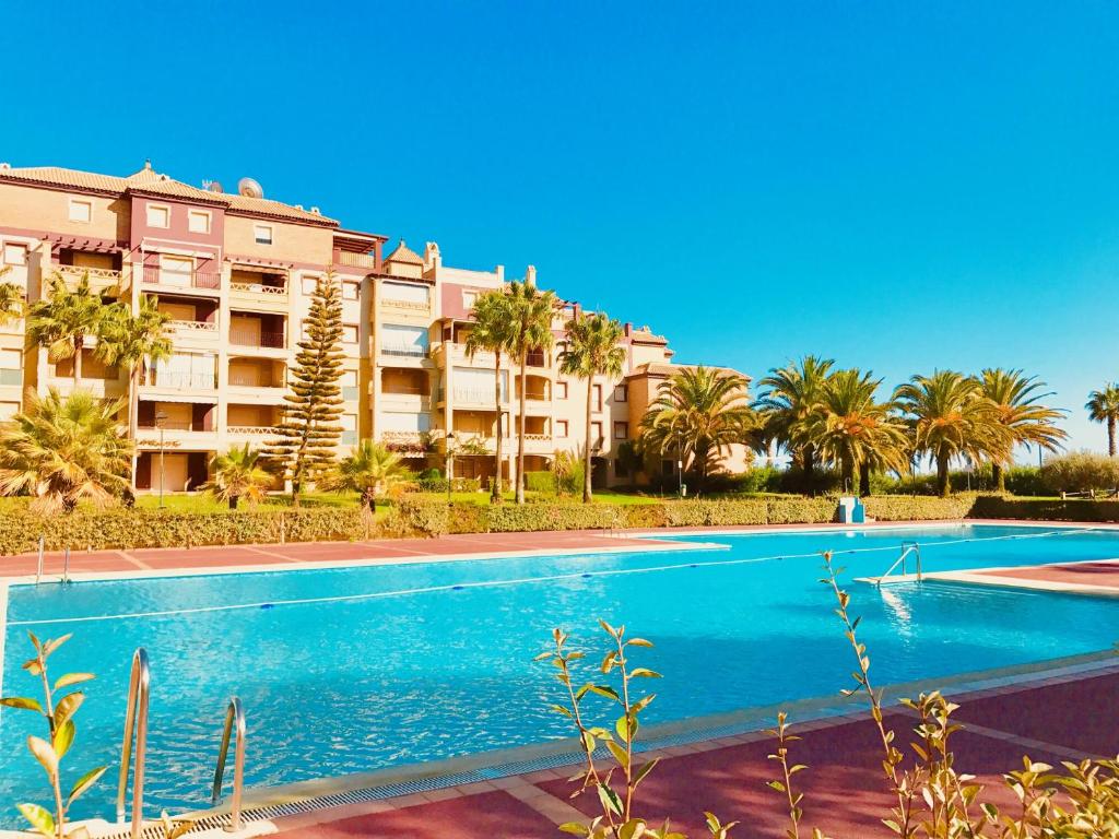 a swimming pool in front of a building with palm trees at Alcaudón, Isla Canela - By AC REAL in Isla Canela