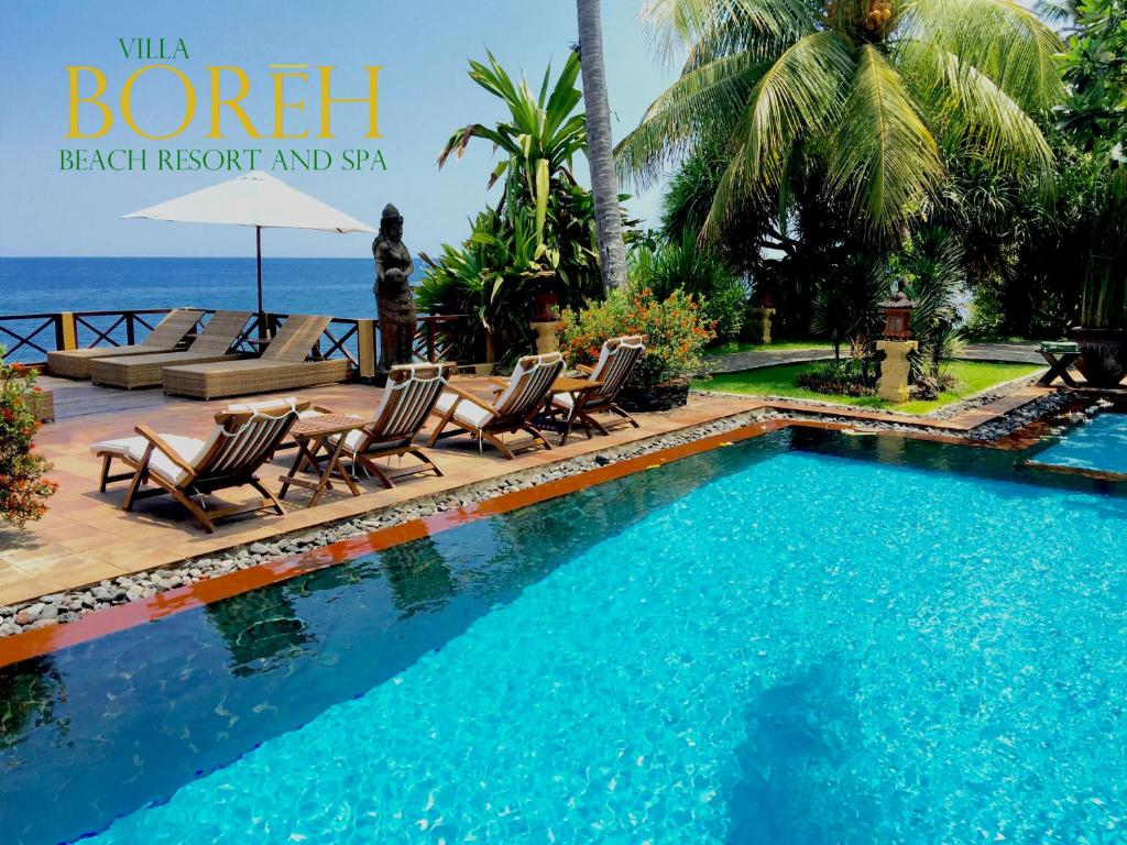 a swimming pool with chaise lounges and chairs next to the ocean at Villa Boreh Beach Resort and Spa in Tejakula