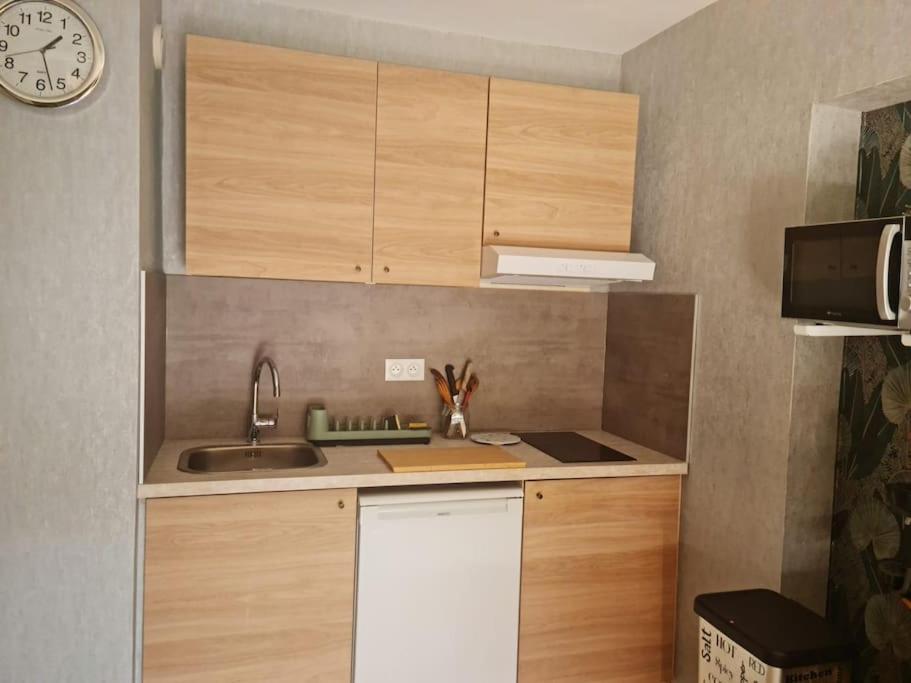 une cuisine avec des armoires en bois et une horloge au mur dans l'établissement Appartement 2 pièces équipé & rénové, à Balaruc-les-Bains