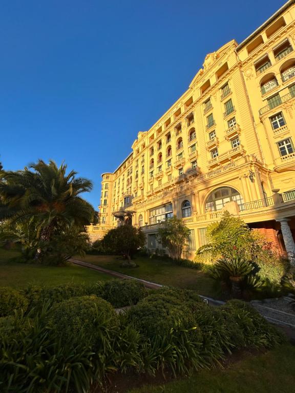 un grand bâtiment jaune avec un palmier devant lui dans l'établissement Sublime Loft dans un Ancien Palace 2 pas de la Mer, à Menton