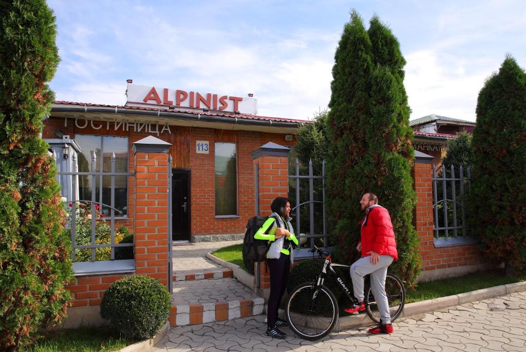 duas pessoas em frente a um edifício com uma bicicleta em Alpinist Hotel em Bishkek