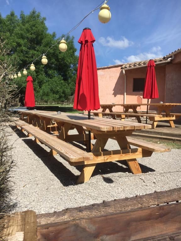 a group of wooden picnic tables with red umbrellas at Domaine privatif 32c avec très grande Salle - Escale de La Jurade in Rogues