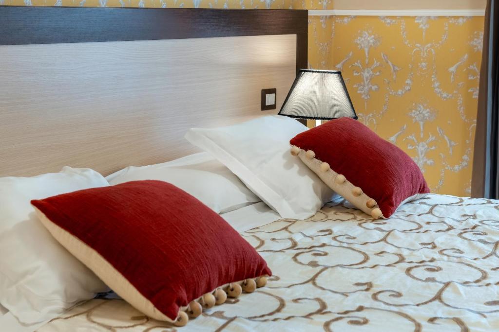 a bed with red pillows and a lamp on it at Hotel De La Ville Relais in Fiumicino