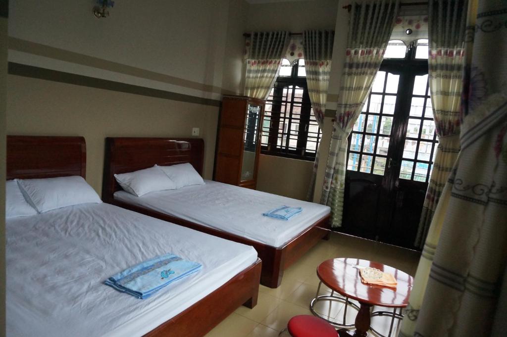 twee bedden in een kamer met twee tafels en ramen bij Thanh Lich Guesthouse in Quang Ngai