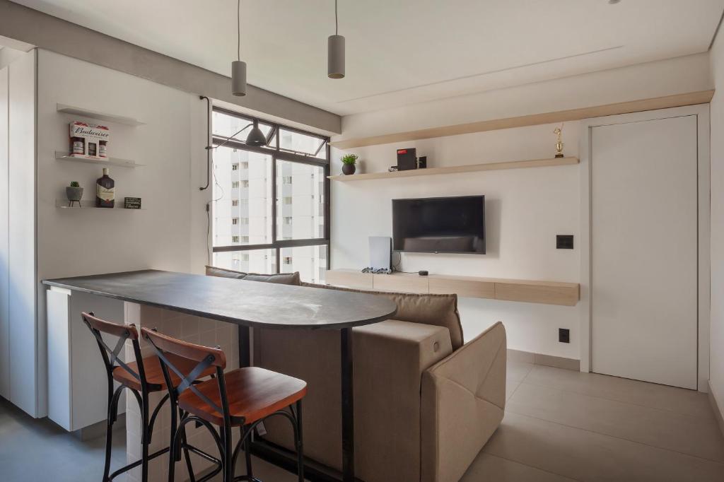 a kitchen with a bar with chairs and a tv at Apartamento Loft Novíssimo in Belo Horizonte