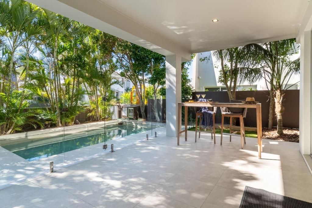 Un patio al aire libre con piscina, mesas y árboles. en Malibu Beach House, en Kingscliff