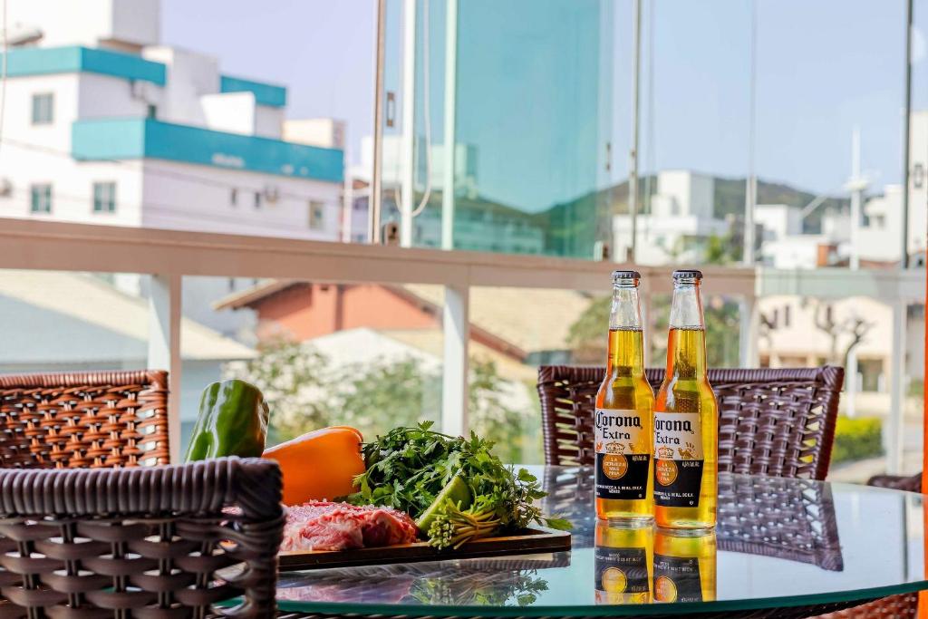two bottles of beer sitting on a table with vegetables at Confortável Apartamento a Poucos Minutos da Praia in Bombas